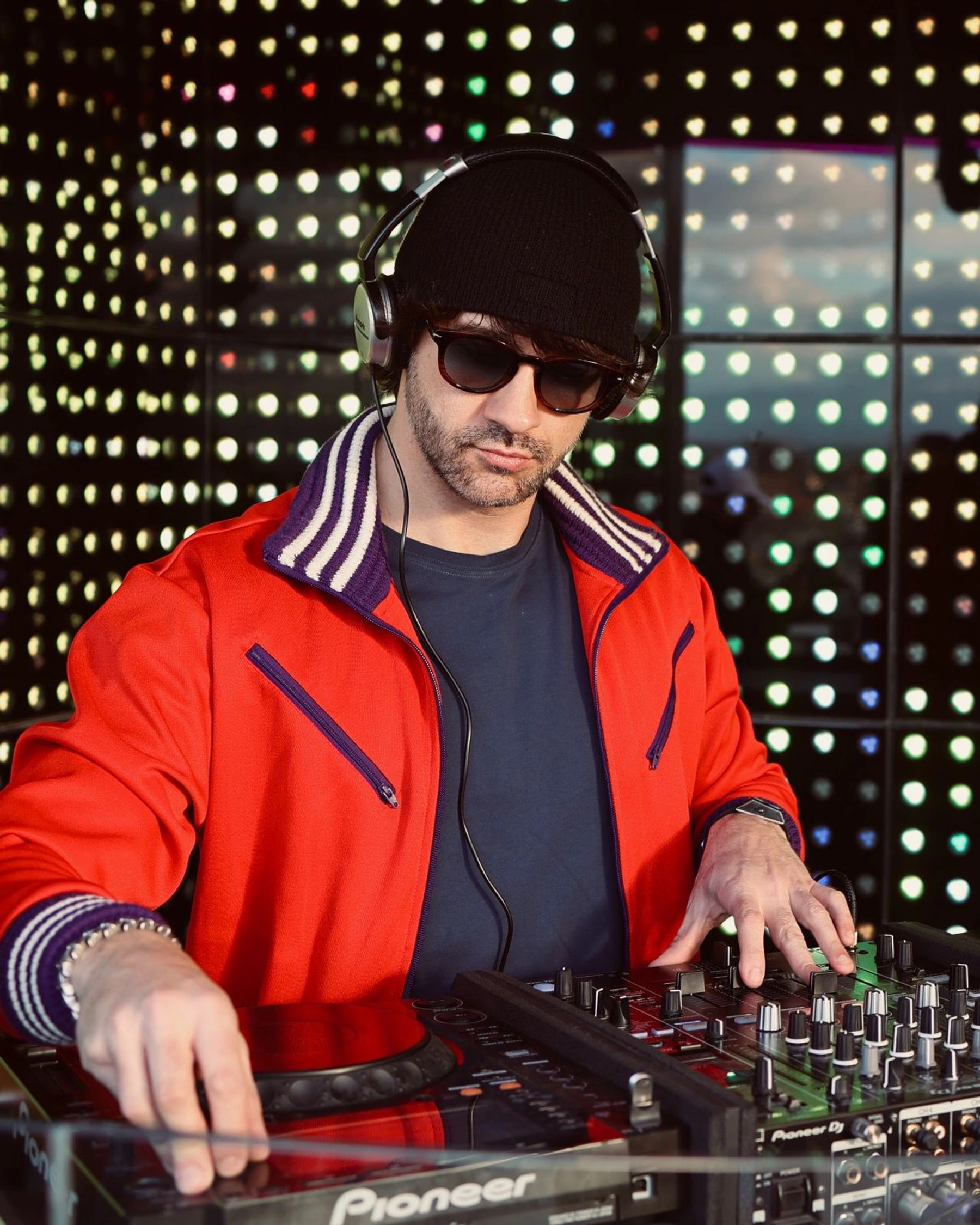 DJ con chaqueta roja frente a una pared de luces