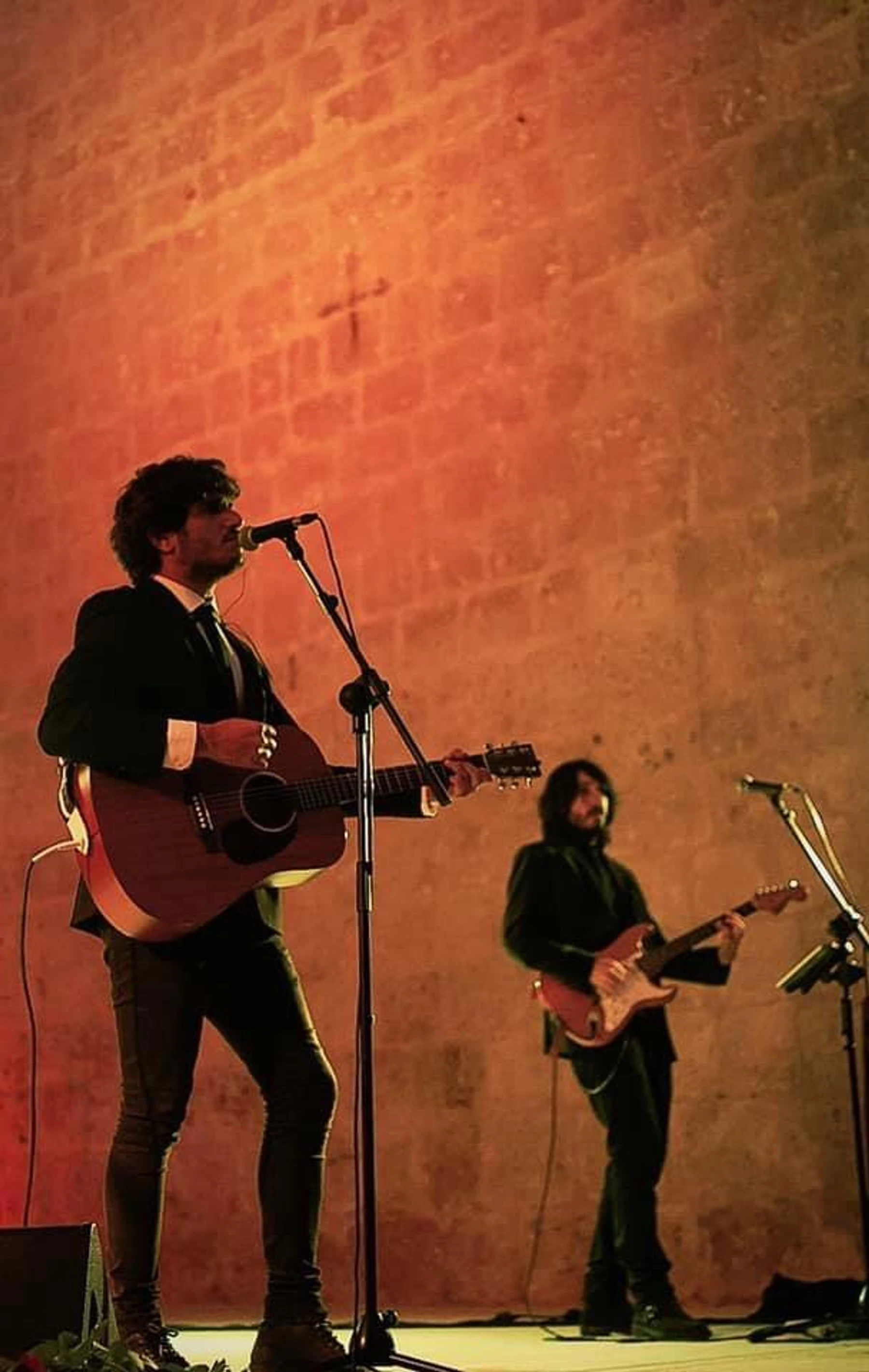 Guitarrista cantando en directo junto a un muro de piedra